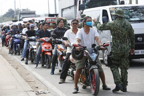 大马尼拉区封城，从黎刹省圣马特奥进入奎松市的摩托车手在警察检查站进行体温检查。